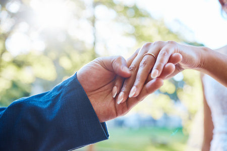 Close up hands of newlywed couple standing outside on a sunny day. Groom holding his brides hand with wedding band. Groom about to put ring in brides fingerの写真素材