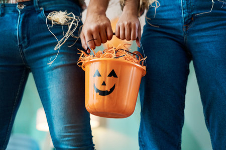 Trick-or-treating together means we get more candy. two unrecognizable people holding a bucket at home.の写真素材