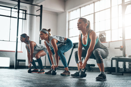 Kettlebell, group and women with fitness, exercise and progress with wellness, balance and workout goal. Female athletes, friends and girls with gym equipment, performance and sports with challengeの写真素材