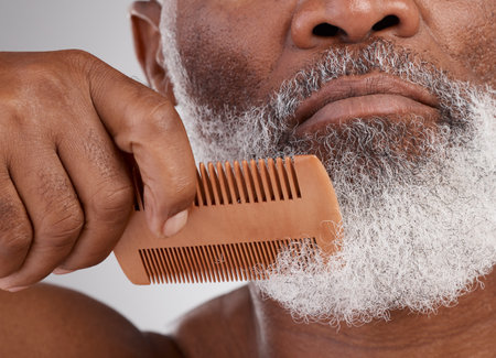 Senior black man, hands and beard with comb in grooming, beauty or skincare hygiene against a studio background. Closeup of African elderly male face combing or brushing facial hair in clean wellnessの写真素材