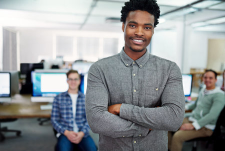 My guys will get the job done. Portrait of a young man standing in an office with designers in the background.の写真素材