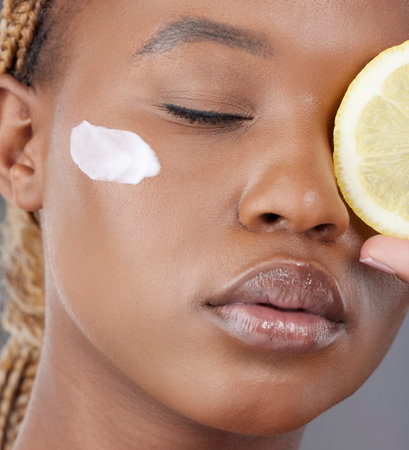 No manifesting, she believes in treatments. Studio shot of an attractive young woman holding a sliced lemon and applying moisturiser to her face.の写真素材