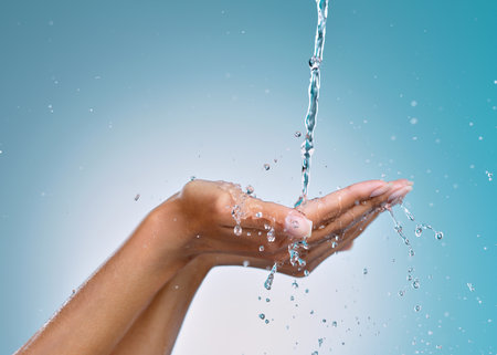 Waiting for the perfect temperature. an unrecognisable woman cupping her hands to catch water against a blue background in the studio.の写真素材