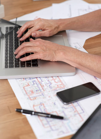 Architect and her tech. Cropped image of an architect working on her laptop with building plans beside her on her desk.の写真素材