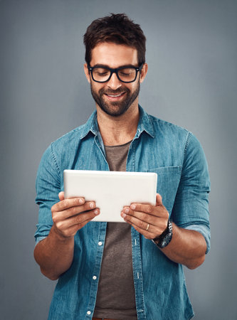 Now theres an app that looks interesting...Studio shot of a handsome young man using a digital tablet against a grey background.の写真素材