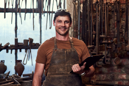 Smart tools and devices are also needed in the workshop. Portrait of a handsome young craftsman using a digital tablet while working inside a metal workshop.の写真素材
