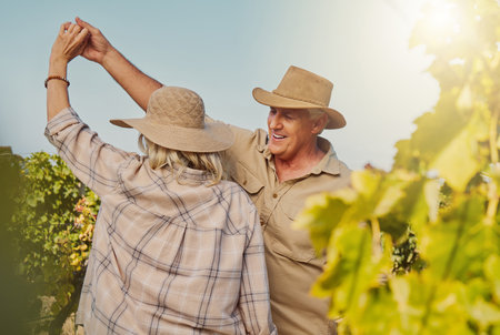 Smiling senior couple dancing together and feeling playful on vineyard. Caucasian husband and wife standing together and enjoying a day on a farm after wine tasting weekend. Man and woman having funの写真素材