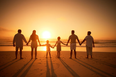 Rear view of multi generation family silhouetted on the beach. Carefree family with two children, two parents and grandparents holding hands and watching the sunset at the beachの写真素材