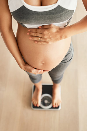 How much have I grown. Cropped high angle shot of a pregnant woman weighing herself on a scale.