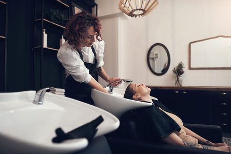 A proper wash rids your hair of all the product buildup. a beautiful young woman getting her hair washed at the salon.の写真素材