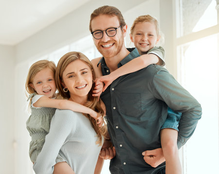 They keep us on our toes. a young couple standing together and bonding with their children by giving them piggyback rides at home.の写真素材