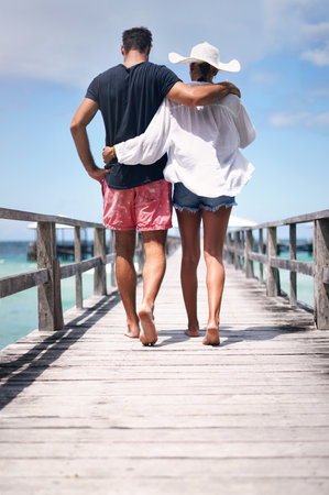 Couple legs, walking and beach deck on a tropical island on vacation with freedom by sea. Ocean, relax and walk of a man back and woman together with love in summer on a holiday outdoor in sunの写真素材