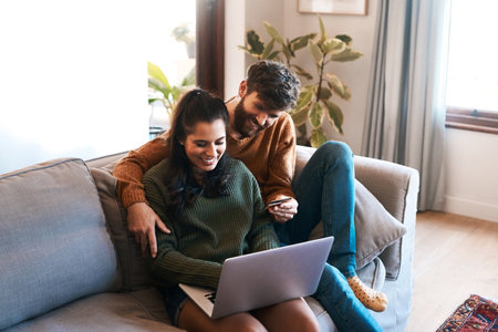 Laptop, credit card and happy couple on sofa, online shopping or cashback and spending in home. Smile, man and woman on couch to relax together, ecommerce or payment with bonding time and happiness.の写真素材