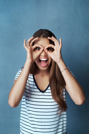 I see it and I love it. Studio shot of an attractive young woman looking through her fingers against a blue background.の写真素材