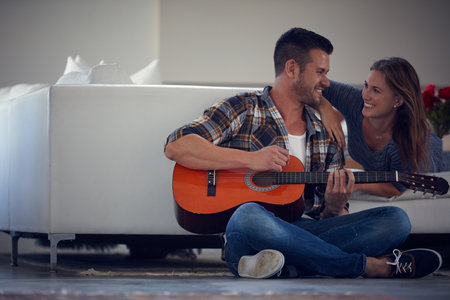 Listening to him play makes me happy. a young married couple spending the day at home.の写真素材