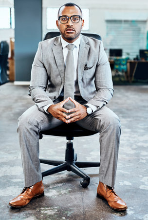 Im ready for the next business venture. Full length portrait of a handsome young businessman sitting alone in his office with his hands together.の写真素材