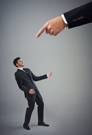 Know your place. Studio shot of a young businessman being reprimanded by a giant hand against a gray background.の写真素材