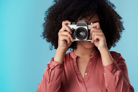 Living life one click at a time. Studio shot of a young woman using a camera against a blue background.の写真素材