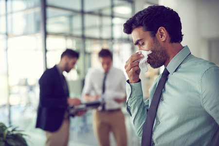 Business, allergies and man with a tissue, sick and healthcare risk with illness, disease and stress. Male person, office and employee cleaning his nose, medical issue and virus with burnout and fluの写真素材
