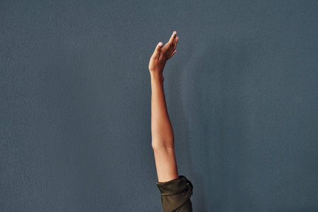 Reach for the top. Studio shot of an unrecognizable woman raising her hand against a grey...