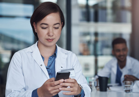 Can I call you sometime. a young female doctor using her smartphone to send a text message.の写真素材