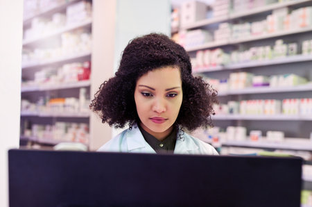 Hard at work for your wellbeing. a pharmacist working on a computer in a pharmacy.の写真素材
