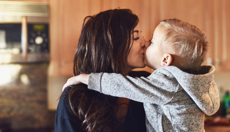 He loves his mommy very much. a cheerful little boy giving his mother a little kiss at home during...