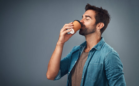 That first sip of coffee...Studio shot of a handsome young man drinking a cup of coffee against a...