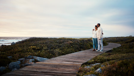 Love, travel and elderly couple hug on a boardwalk at a beach, calm and content against blue sky background. Senior, man with woman on ocean trip, holiday or vacation, happy and enjoying retirementの写真素材