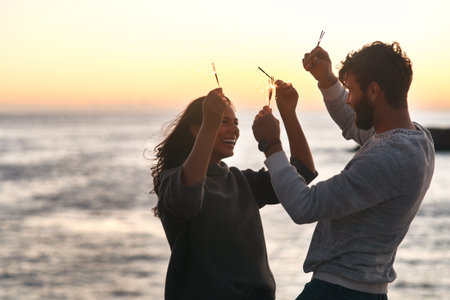 Sunset, beach and couple with sparklers for celebration, party and quality time on romantic date....