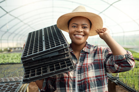 Happy farmer carrying empty trays. African american farmer working in a greenhouse. Young farmer...