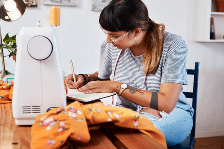 I make notes throughout the whole process. a young woman making notes while designing a garment at home.の写真素材
