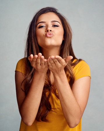 Here, catch my mwah. Studio portrait of an attractive young woman blowing a kiss against a grey background.の写真素材