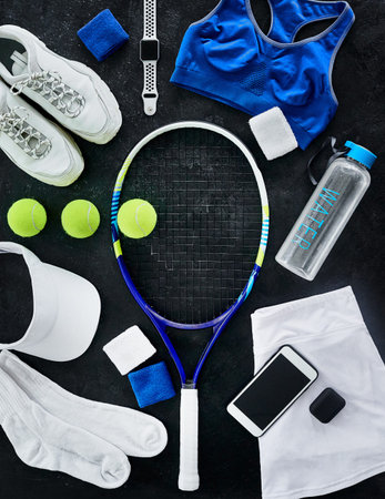 High angle shot of tennis essentials placed on top of a dark background inside of a studio.