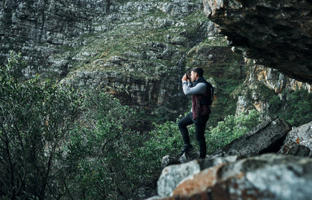 Climb the mountain so you can see the world. a young man taking photos while out on a hike.の写真素材