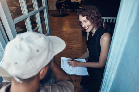 Do I need to sign anywhere else. High angle shot of an attractive young hairdresser signing for a delivery from the courier at her salon.の写真素材