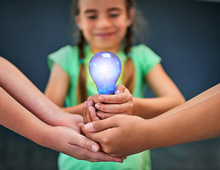 Learning leads to action. a group of kids holding a lightbulb together.の写真素材