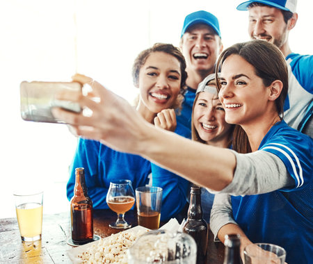 Catching the game with the crew. a group of friends taking a selfie while watching a sports game at...