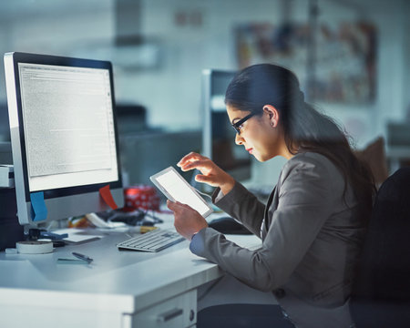 Online and on the job. Shot of a young businesswoman working late in the office.の写真素材