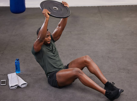 Black man holding weight plate for fitness, exercise and workout in gym. Strong bodybuilder...