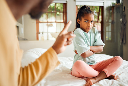 Scolding, angry and kid on bed in home with unhappy, annoyed and tantrum expression. Serious conflict, problem and upset father in black family disappointed with young child in house.の写真素材