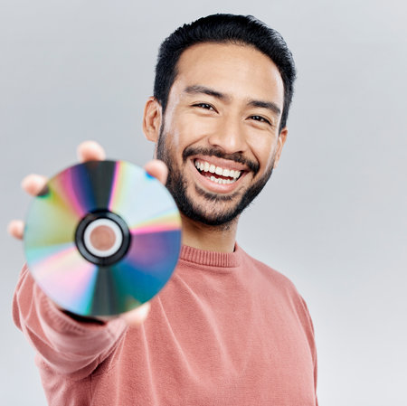 Happy, showing and portrait of an Asian man with a cd isolated on a white background in a studio. Smile, excited and a Japanese person with a copy of multimedia, music or a movie on a backdropの写真素材