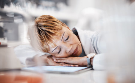 Scientist sleeping, tired and overwork with woman and burnout with insomnia from overtime. Medical research, scientific innovation and senior female in science, fatigue and overwhelmed in laboratoryの写真素材