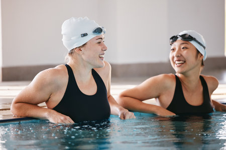 Swimming pool, sports and women laughing in water, joke and funny comedy after exercise. Swimmer, happiness and friends or girls talking, laughter and comic discussion with humor after training.の写真素材
