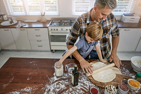 Add some more flour...a father and his son making pizza at home.の写真素材