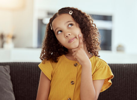 Thinking, young girl and home with ideas and inspiration on a living room sofa. Cute, decision and child with an idea and option consideration on a lounge couch in a house with youth and weekend planの写真素材