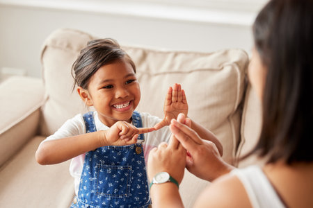 Sign language, learning and girl kid with her mother in the living room of their family home. Happy, smile and child speaking with her hands to her deaf mom to communicate in their modern house.の写真素材