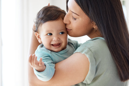 Mom, kiss and holding baby in home for love, care and quality time together to nurture childhood development. Mother, kissing and carrying infant girl kid for support, happiness and comfort of parentの写真素材