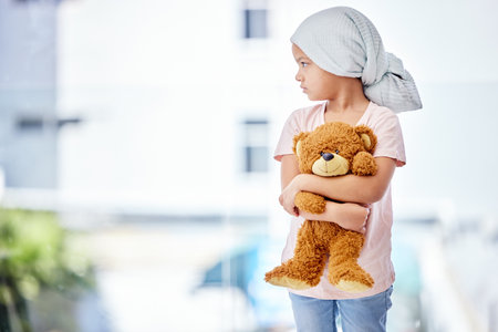 Healthcare, teddy bear and child cancer patient holding her toy for support or comfort. Medical, recovery and girl kid with leukemia standing after treatment or chemotherapy in a medicare hospital.の写真素材