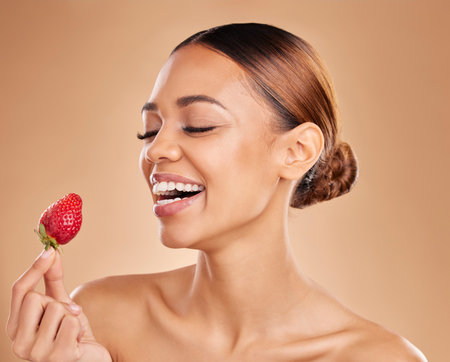 Beauty, skincare or happy woman with strawberry in studio on beige background for healthy nutrition or clean diet. Smile, face or funny girl model laughing or marketing natural fruits for wellnessの写真素材